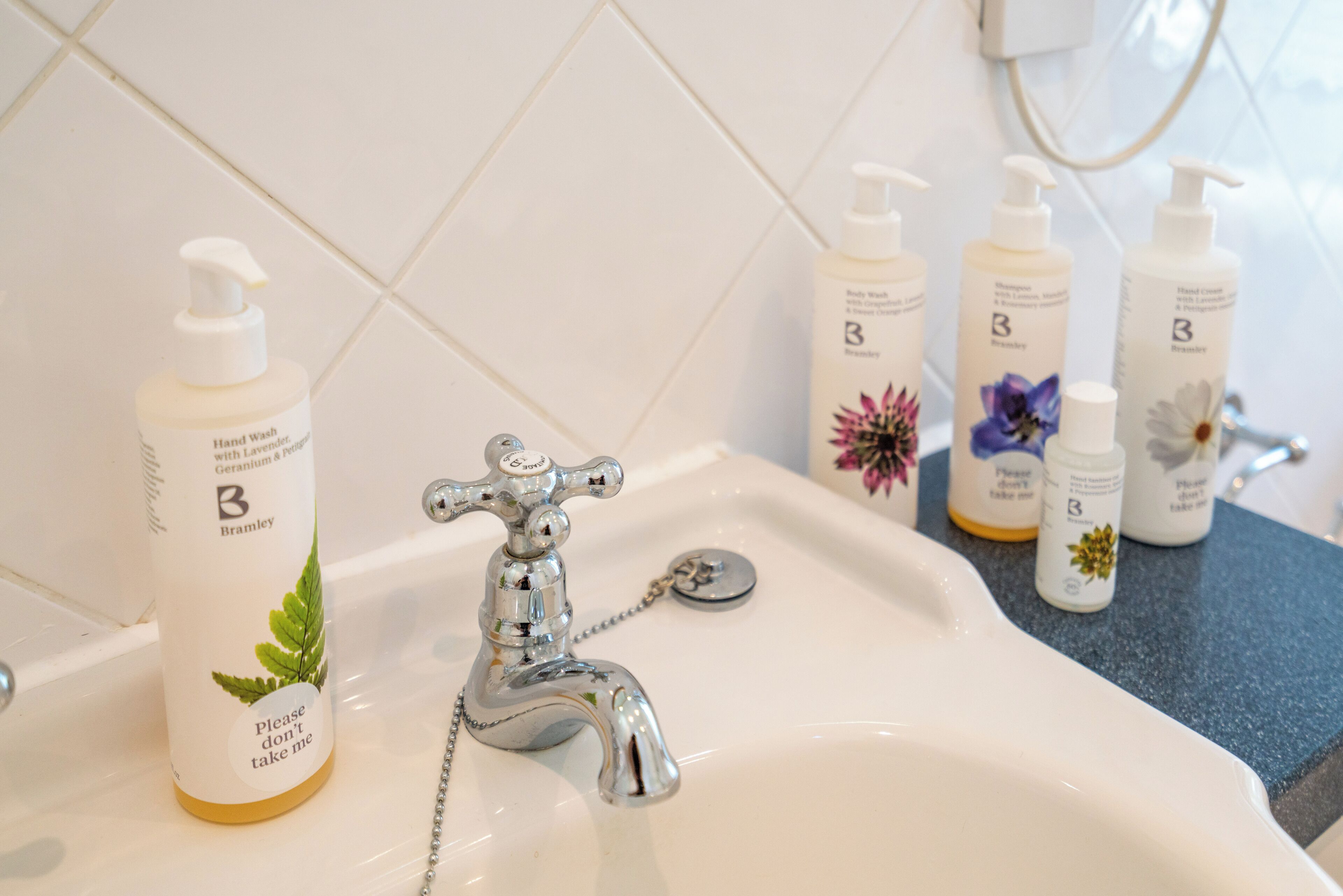 A bathroom sink with a chrome faucet, a hand soap dispenser, and several bottles of hand cream.