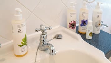 A bathroom sink with a chrome faucet, a hand soap dispenser, and several bottles of hand cream.
