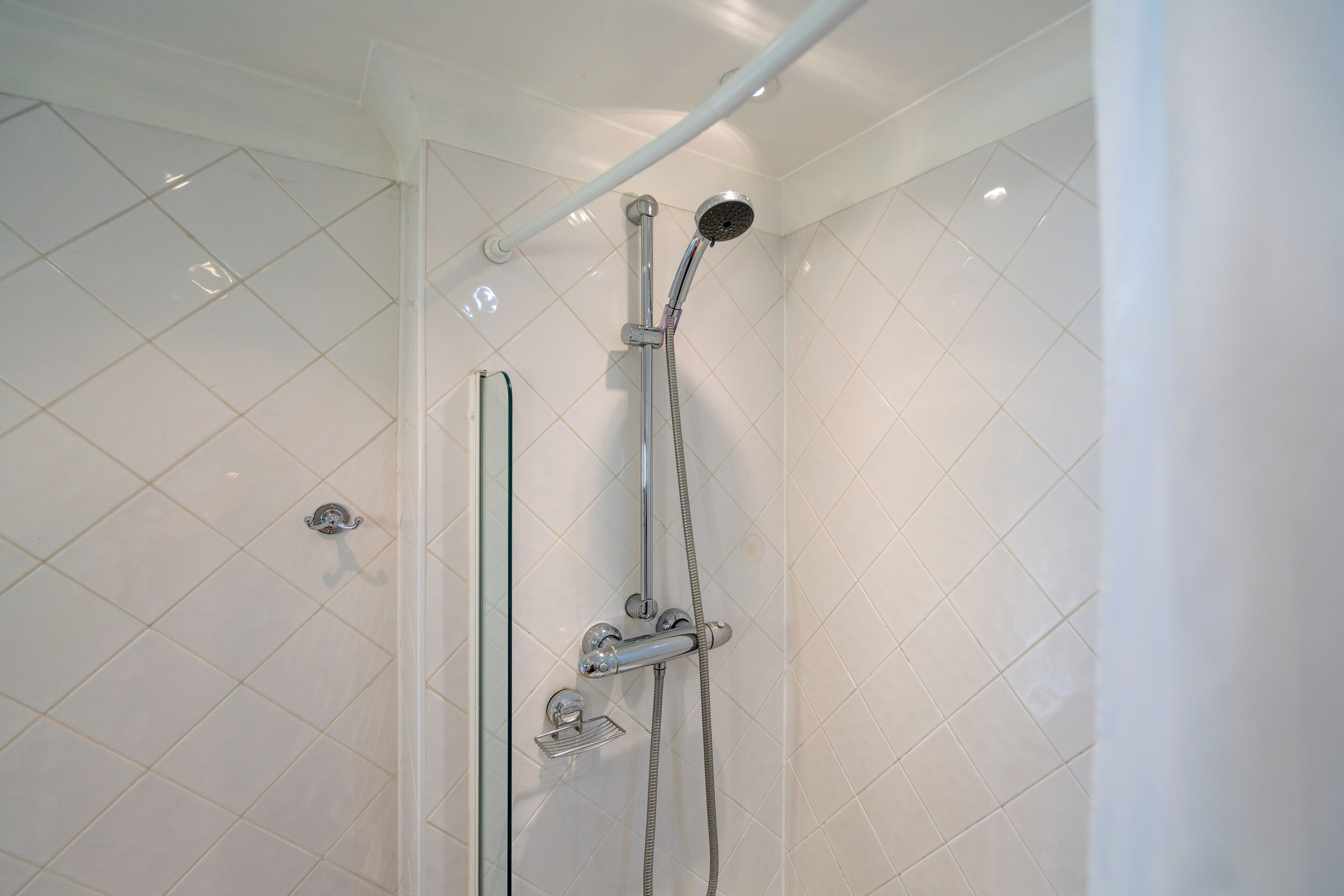 A shower with a handheld showerhead and a wall-mounted faucet.