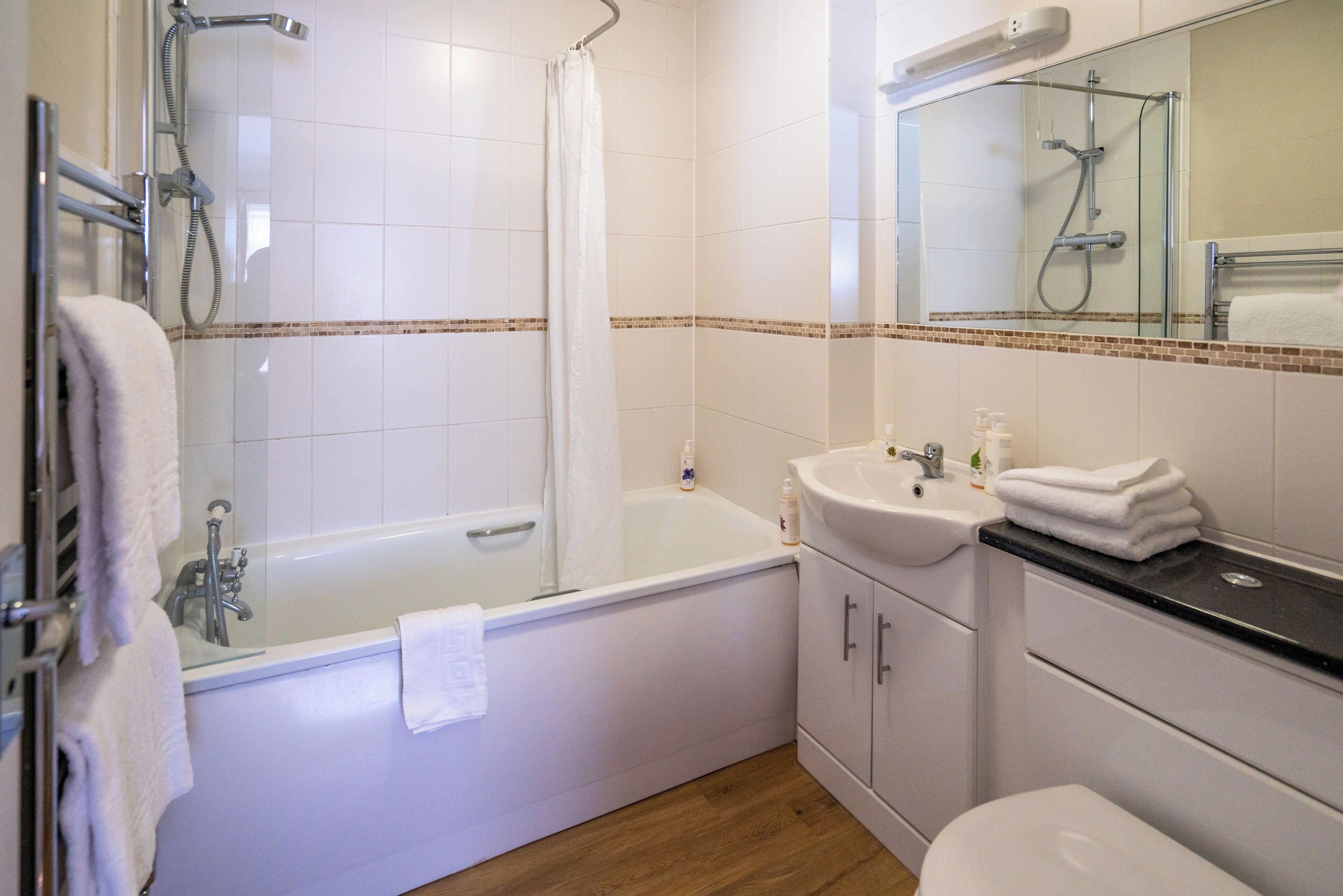 A modern bathroom with a glass-enclosed shower, a white bathtub, a sink with toiletries, and a toilet.