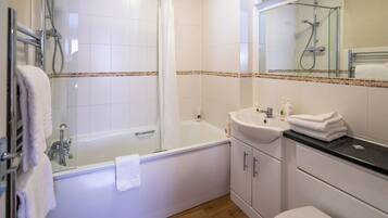 A modern bathroom with a glass-enclosed shower, a white bathtub, a sink with toiletries, and a toilet.