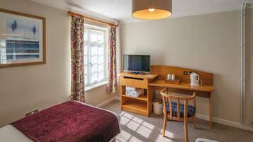 A hotel room with a bed, a desk with a computer, a chair, and a window with curtains.