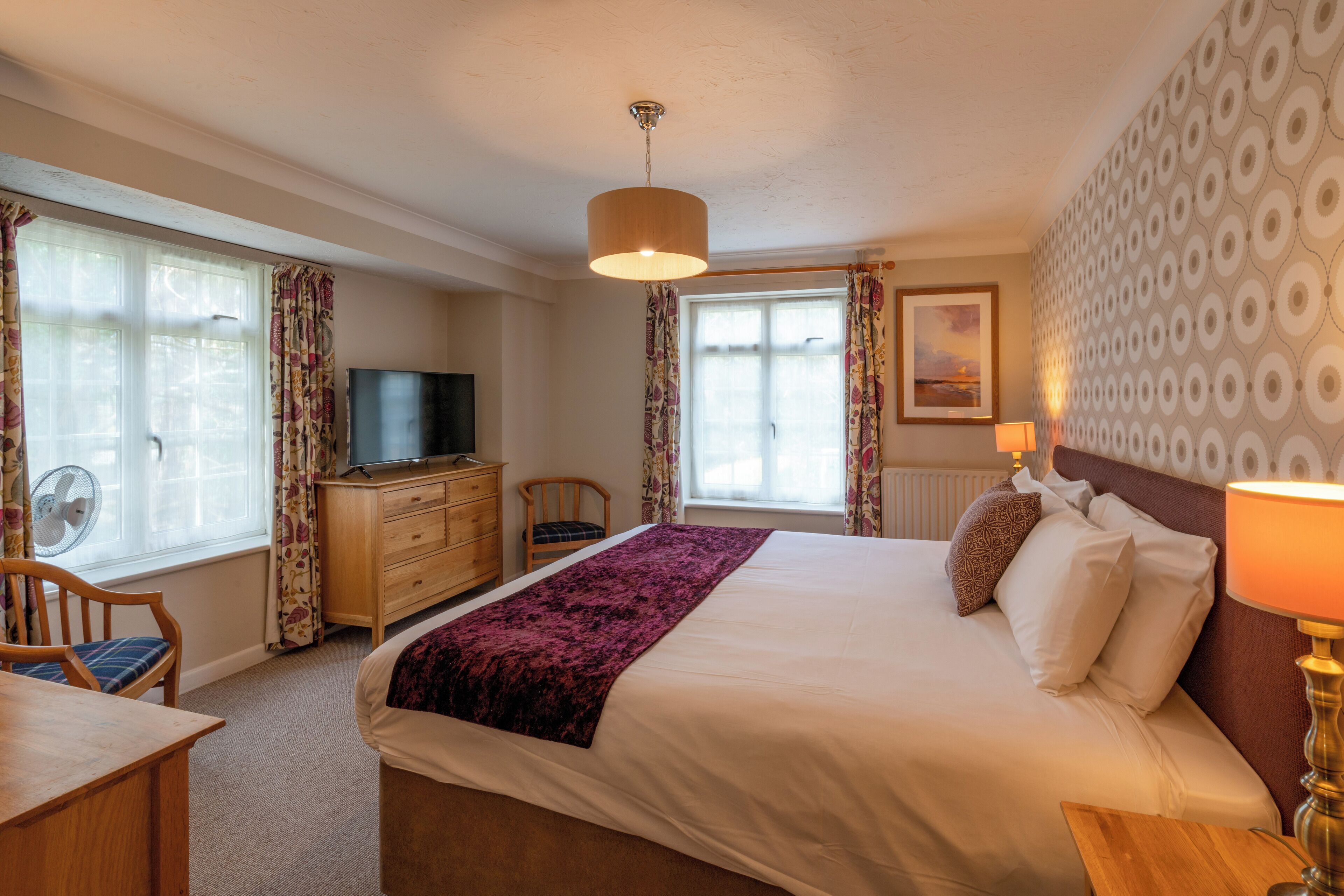 A hotel room with a bed, a desk, a chair, a television, and a window with curtains.