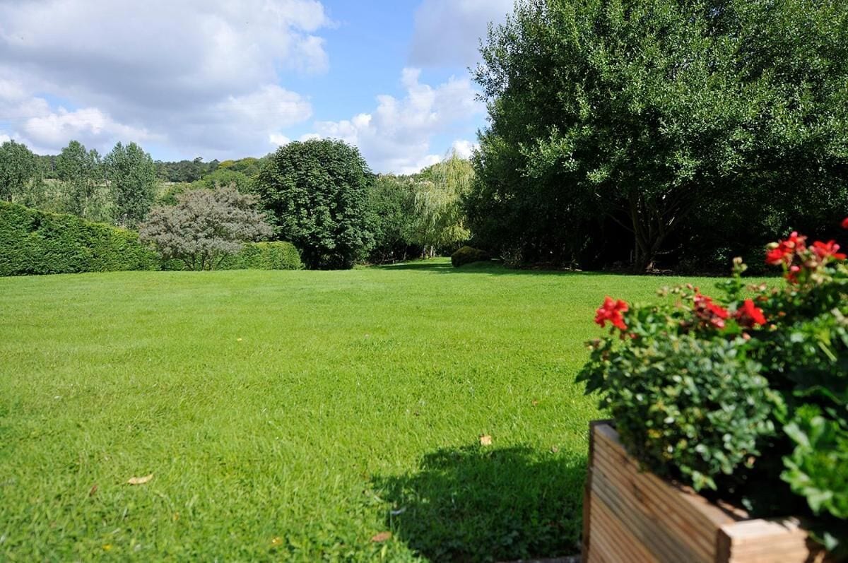Un campo cubierto de césped bien cuidado con una jardinera de madera que contiene flores rojas en primer plano.