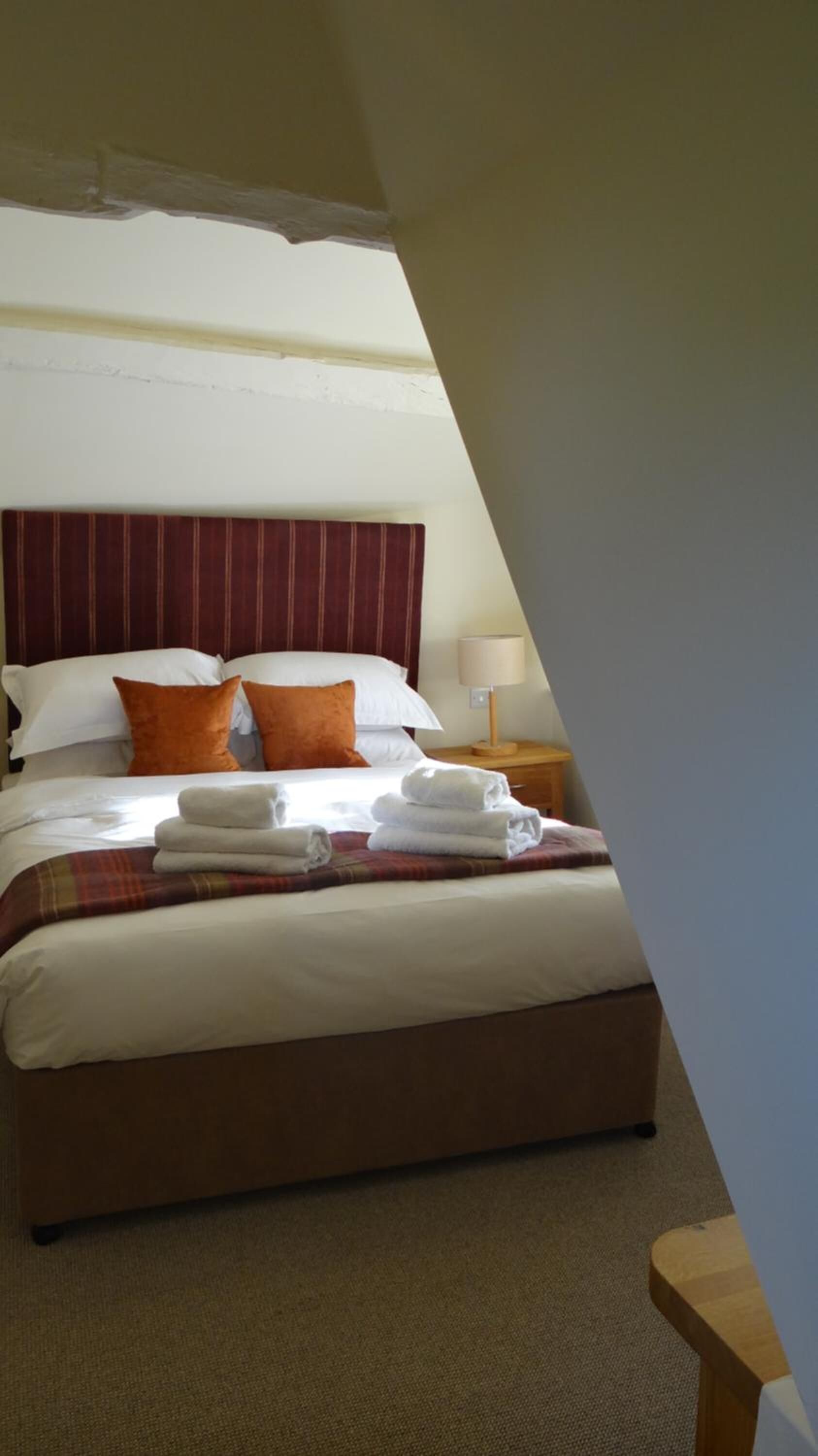 Una habitació d'hotel amb un llit gran, un panell de capçalera a ratlles i una tauleta de nit amb una làmpada.
