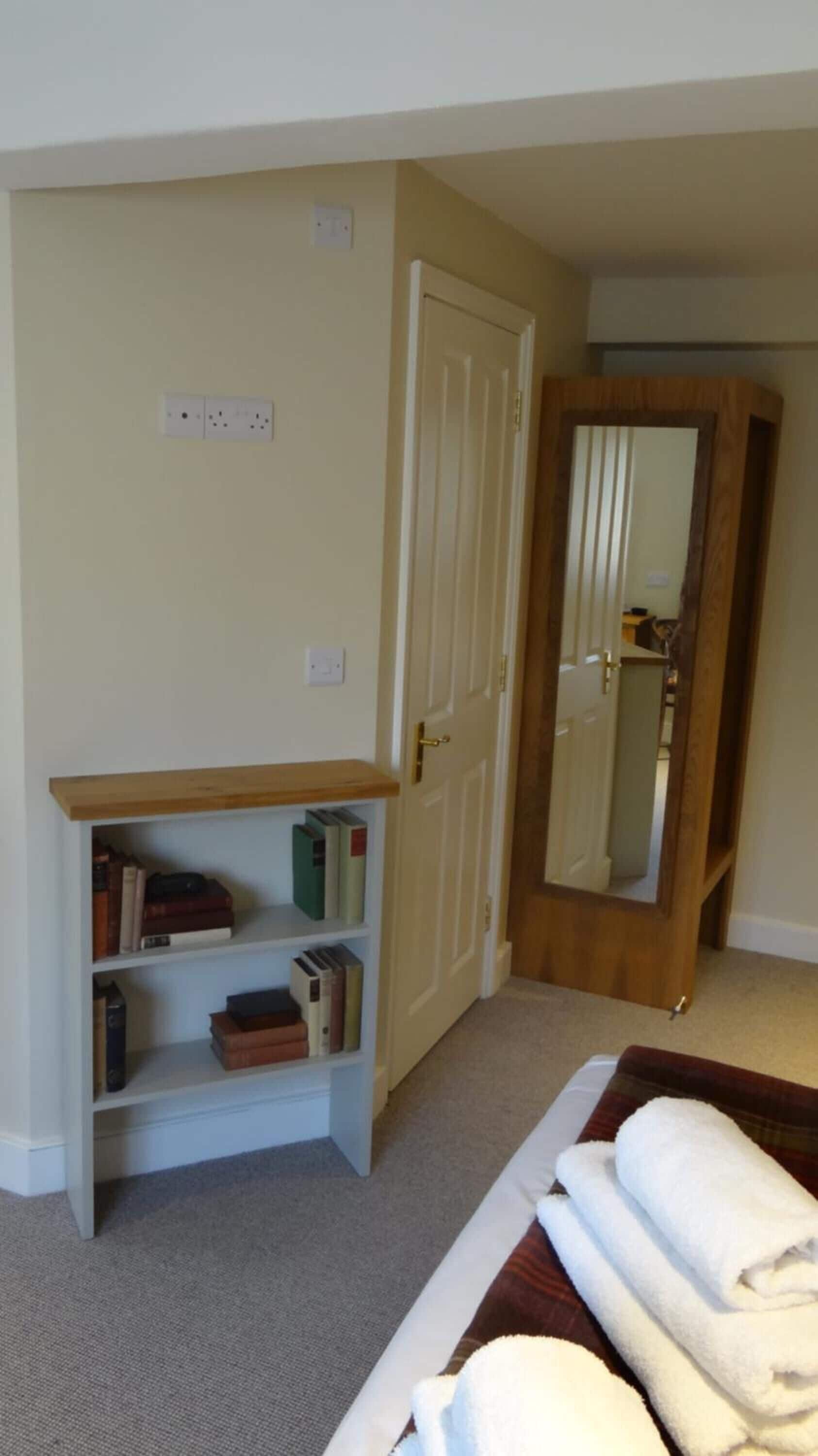A bedroom with a bed, a bookshelf, a door, and a mirror.