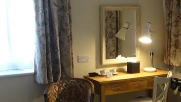 Een kamer met een houten bureau, een stoel, een bureaulamp, een spiegel en een raam met gordijnen.