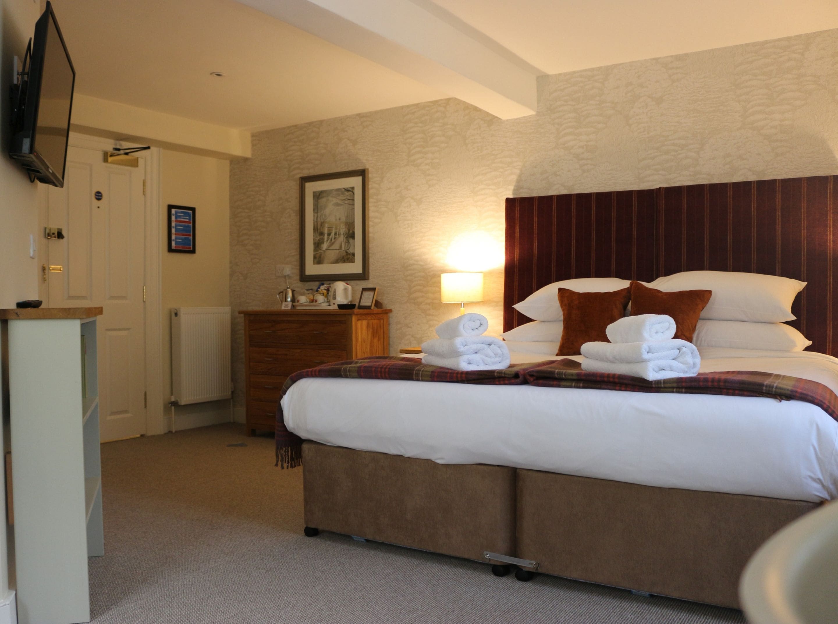 A hotel room with a bed, a dresser, a television on the wall, and a framed picture above the dresser.