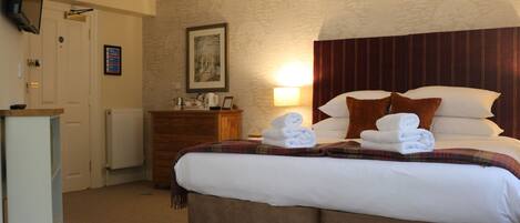 A hotel room with a bed, a dresser, a television on the wall, and a framed picture above the dresser.