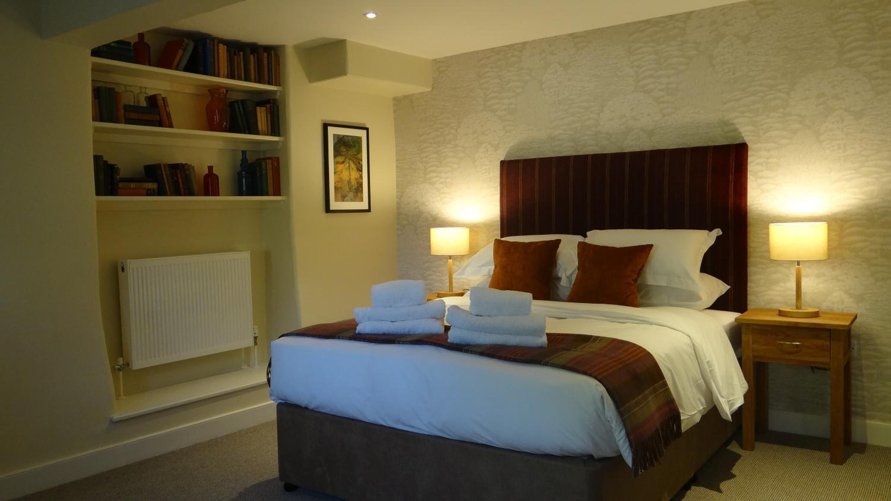 Una habitación de hotel con una cama grande, dos lámparas de noche, una estantería y un cuadro en la pared.