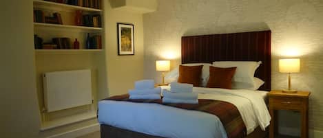 A hotel room with a large bed, two bedside lamps, a bookshelf, and a framed picture on the wall.