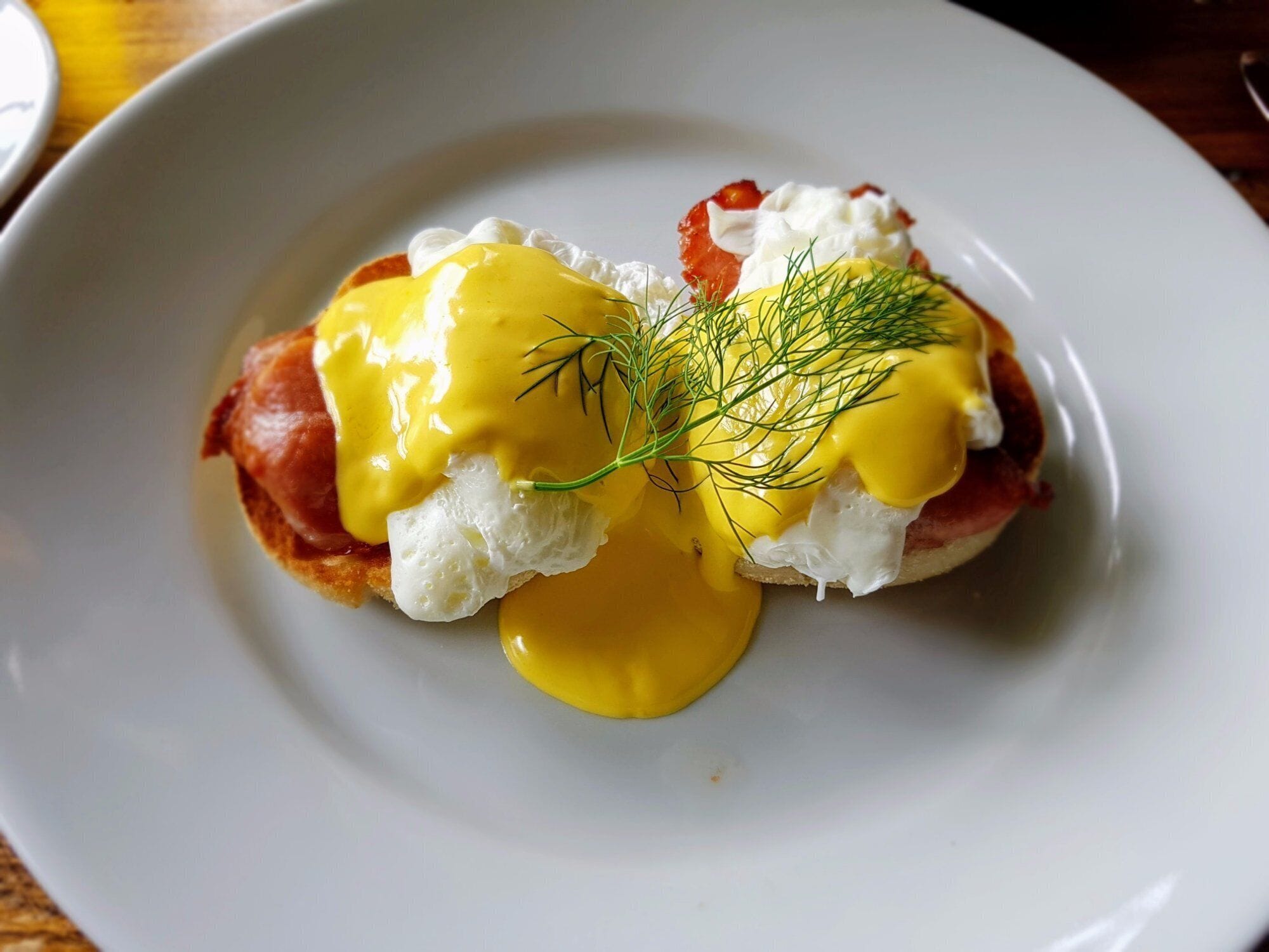 Un plato con un guiso de huevos, jamón y salsa holandesa, adornado con eneldo.