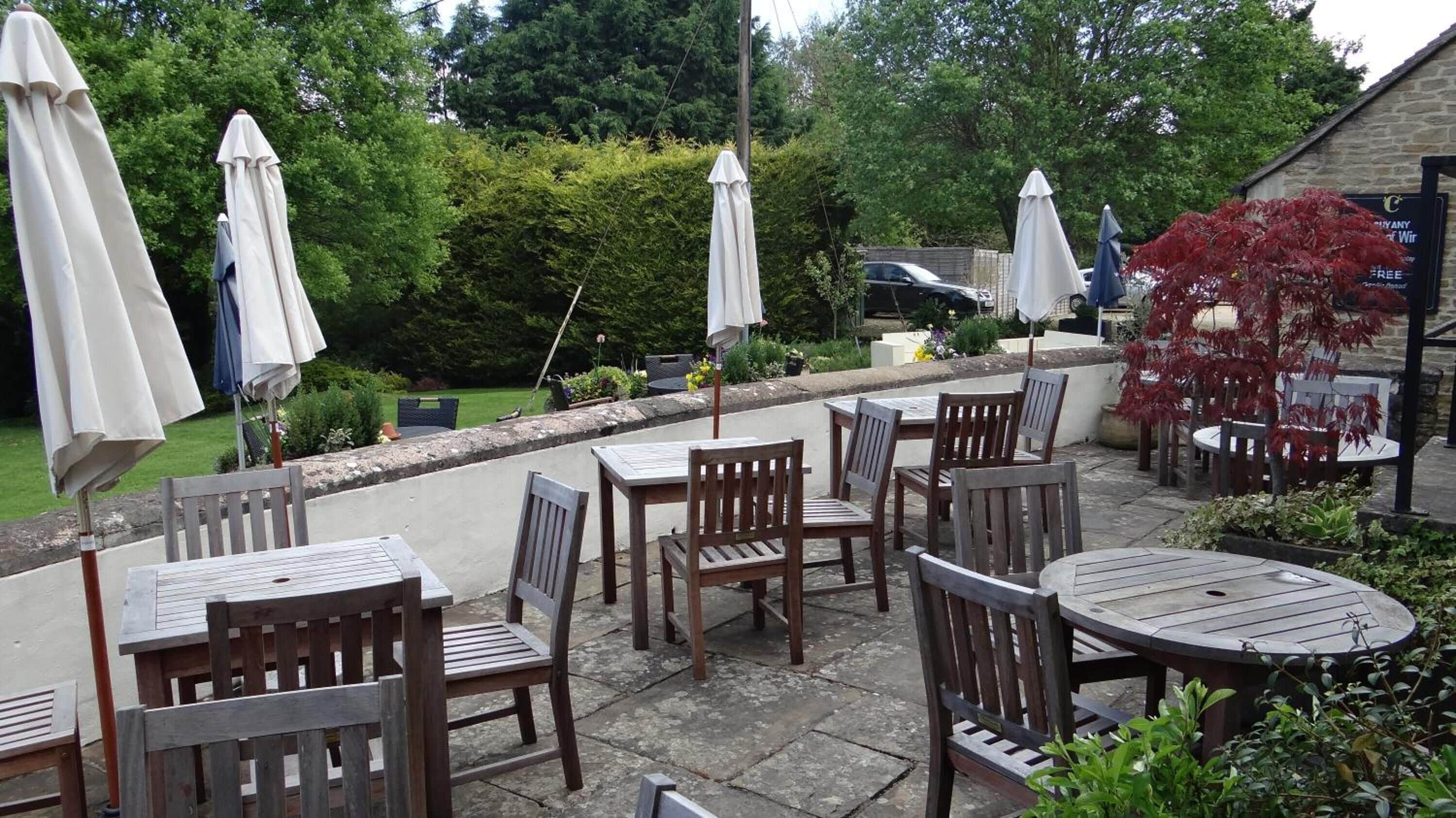 An outdoor patio with wooden tables and chairs, white umbrellas, and a stone wall.