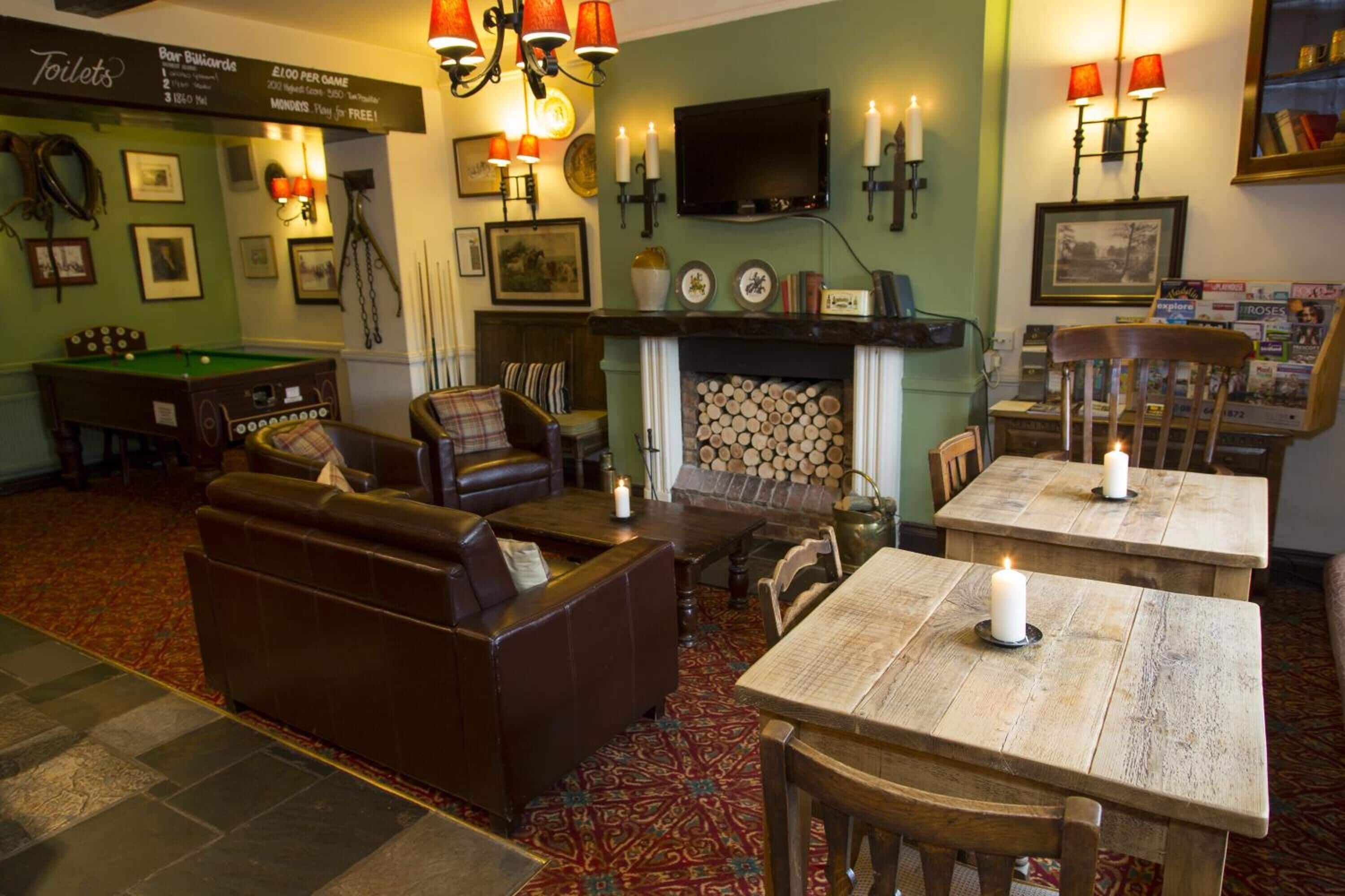 A cozy pub with a billiards table, leather seating, a fireplace, and a television mounted on the wall.