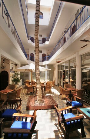 A multi-level indoor space with wooden furniture, a central palm tree, and a checkered floor pattern. - Hotel La Residence (St. Louis)
