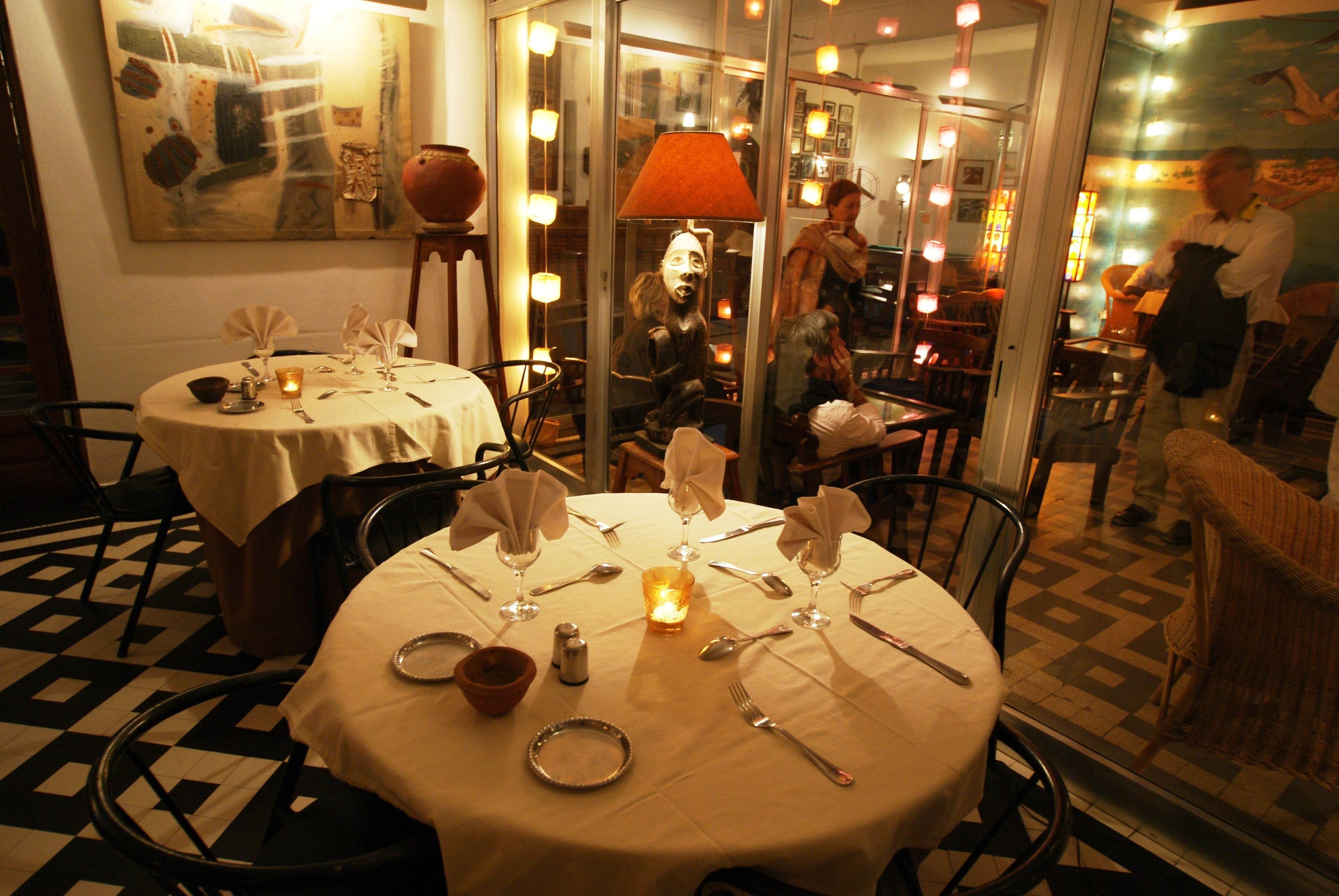 A restaurant with round tables set for dining, a glass partition, and a decorative lamp.