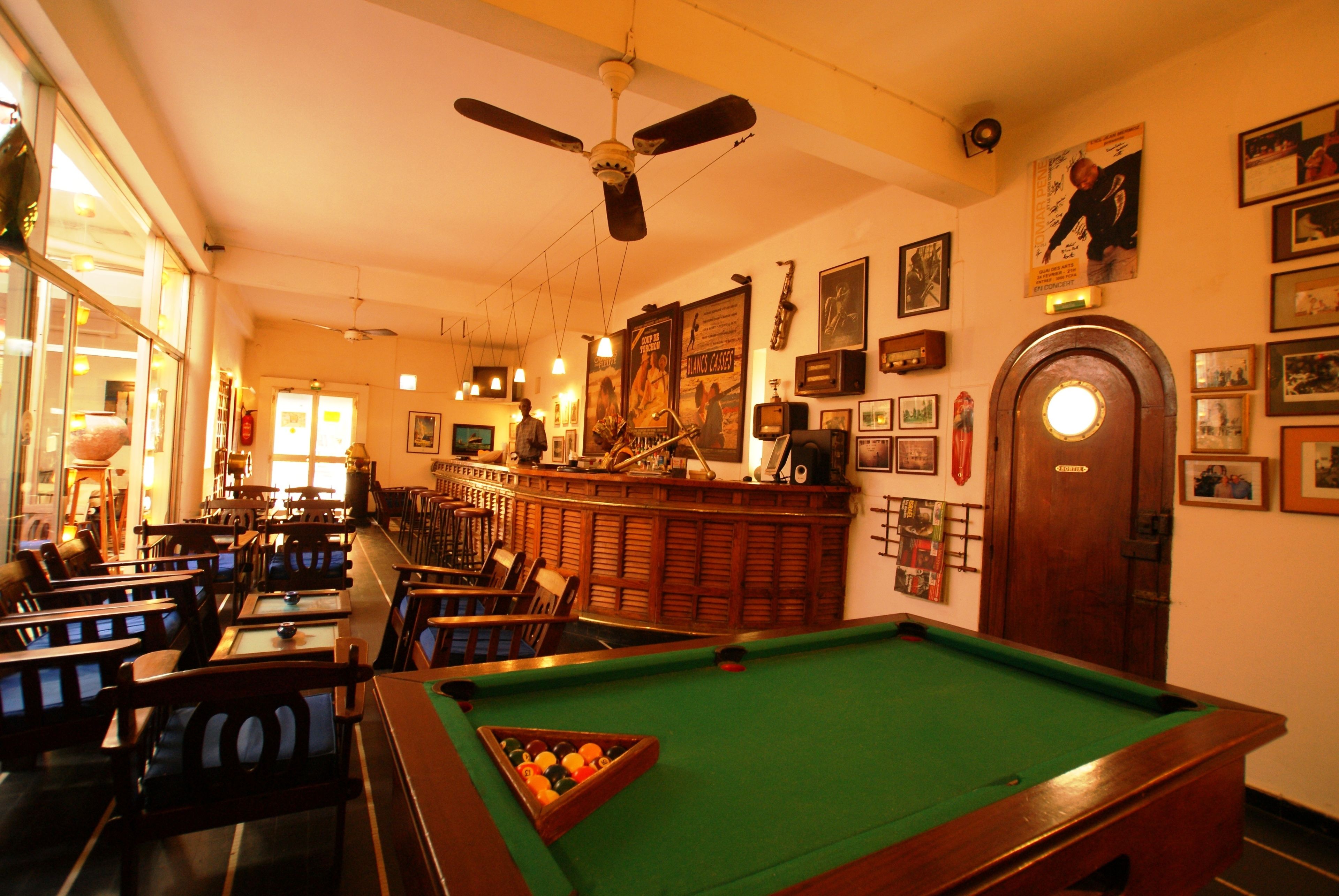 A billiards room with a pool table, chairs, and a bar area.