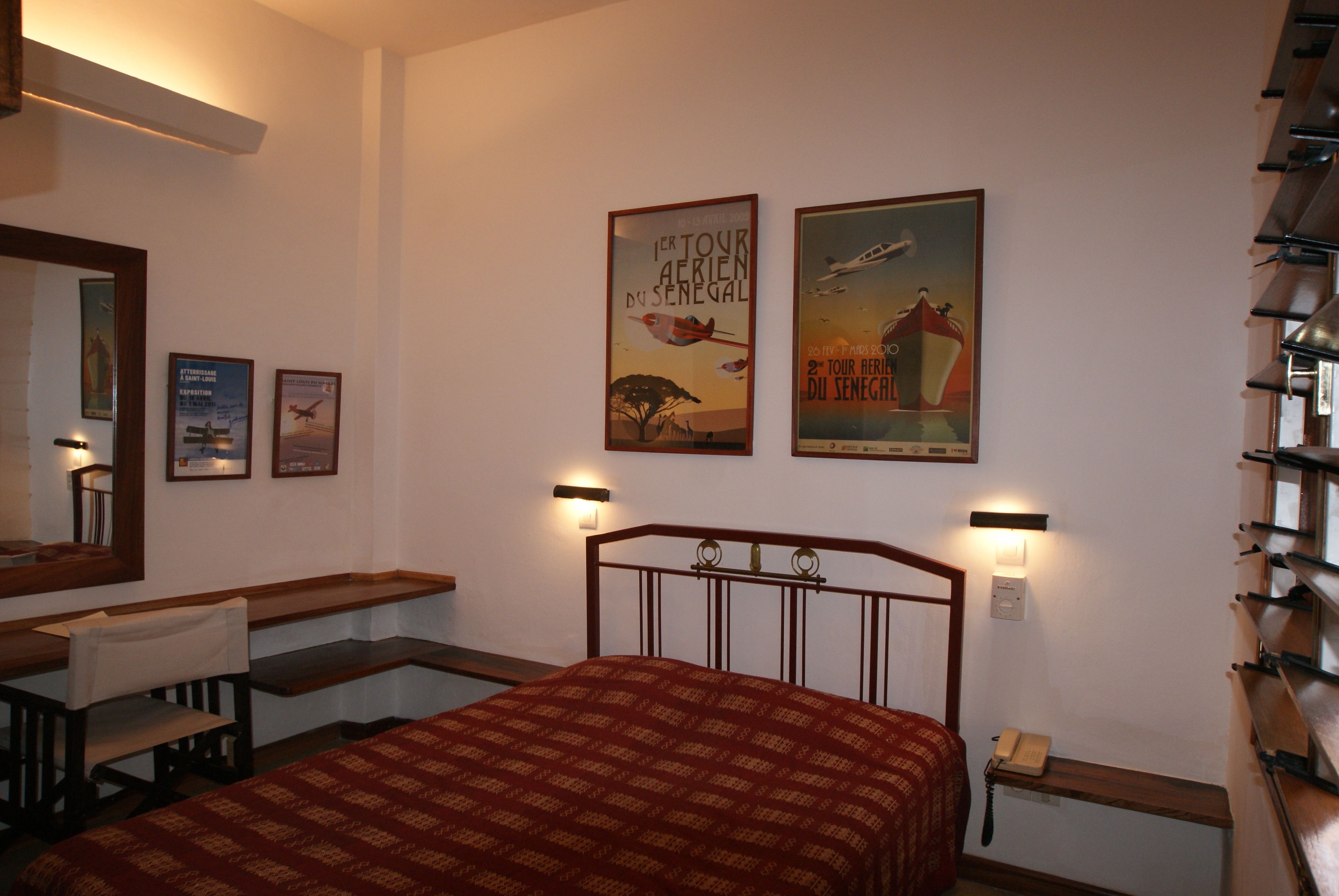 A hotel room with a bed, a desk, a chair, a mirror, and two posters on the wall.