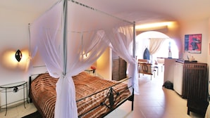 A four-poster bed with a canopy, a small bedside table, a chair, a desk, and a poster on the wall. - Hotel La Residence (St. Louis)