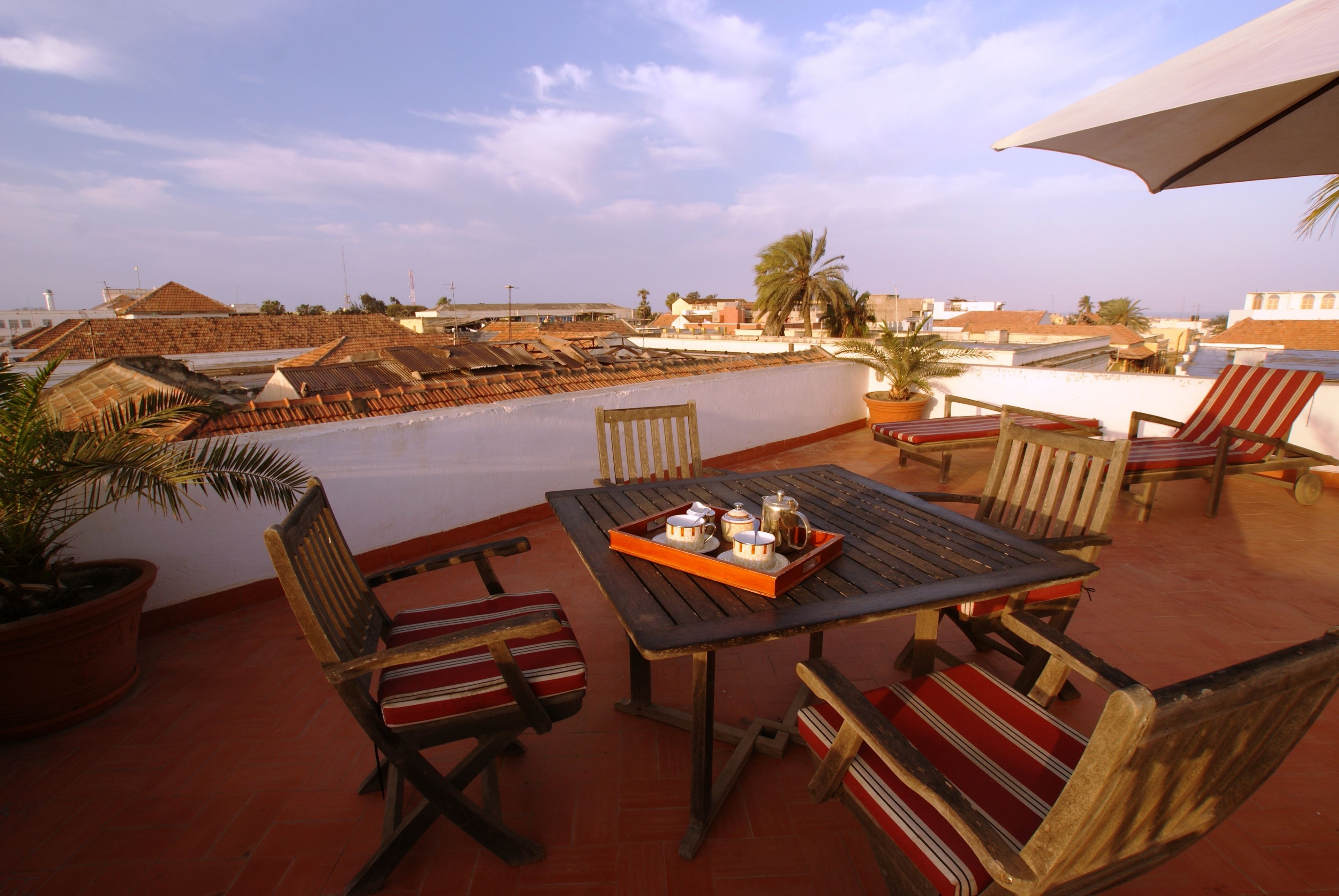 A rooftop terrace with a table set for two, surrounded by wooden chairs with striped cushions.