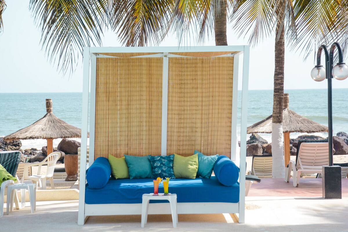 Un salon de plage avec un canapé bleu, une petite table avec des boissons et des parasols en chaume.