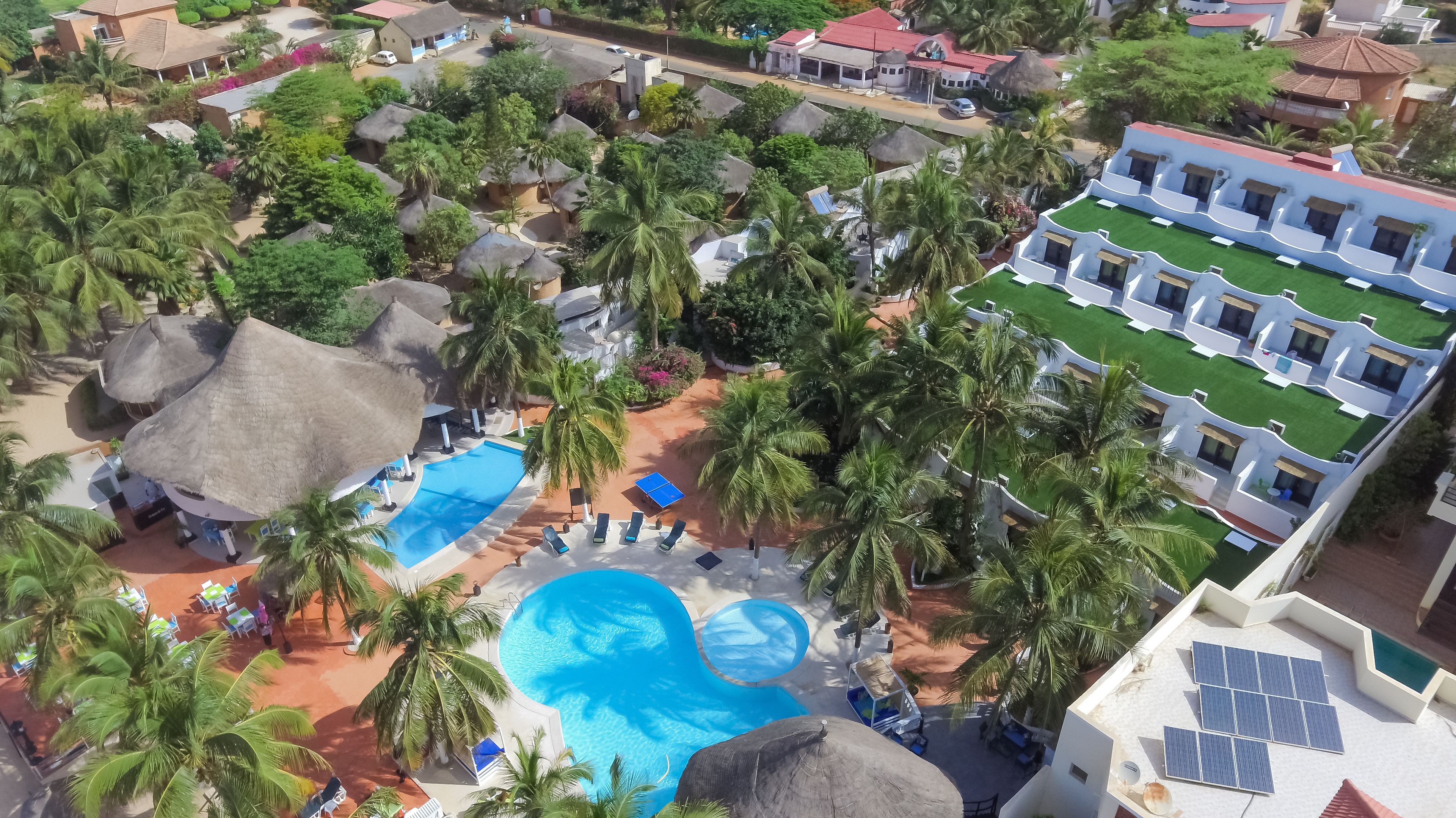 Vista aérea de un complejo turístico con piscina, palmeras y un edificio de varios balcones.