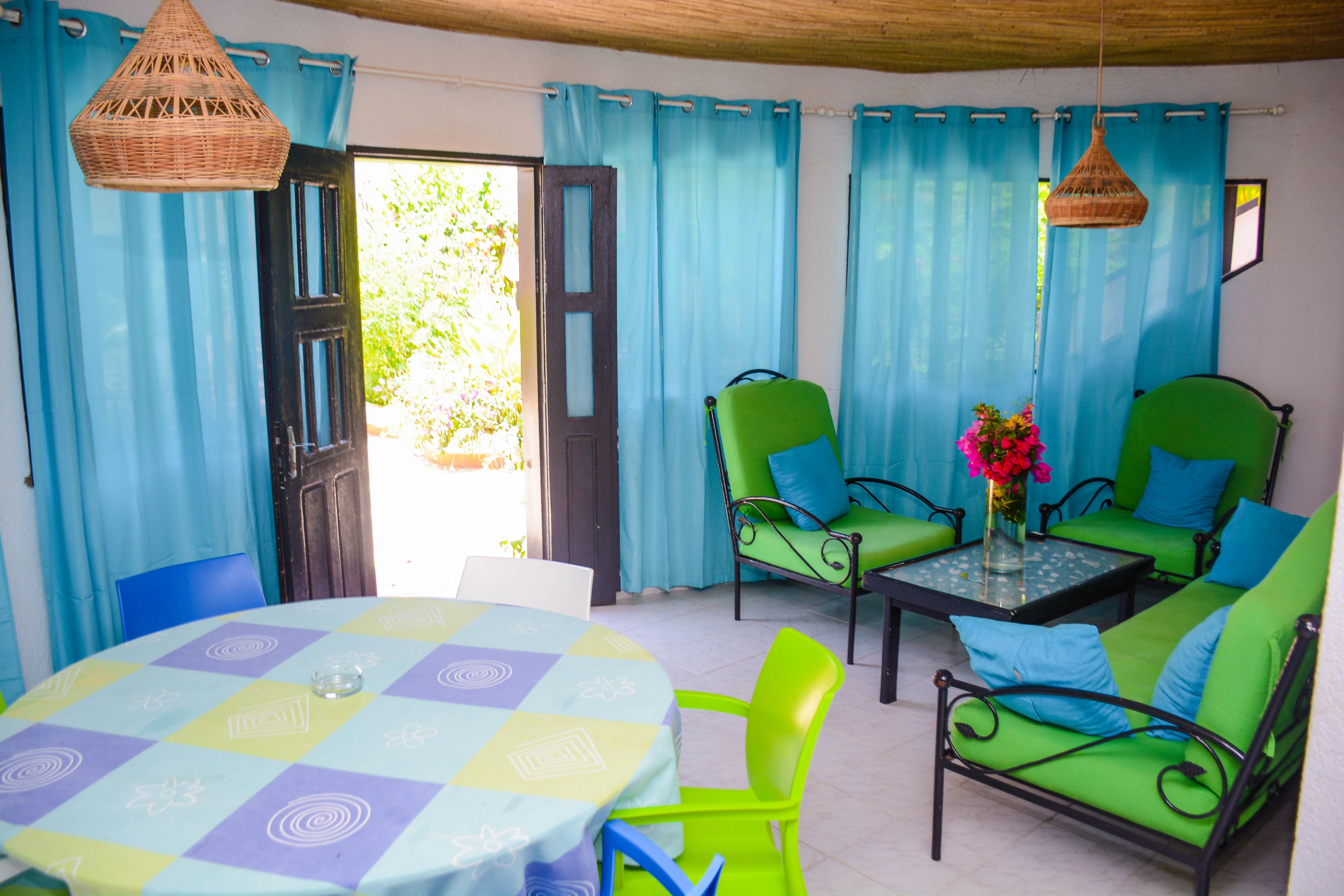 A room with a round table, green chairs, and a sofa with blue cushions.