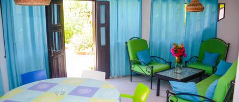 A room with a round table, green chairs, and a sofa with blue cushions.