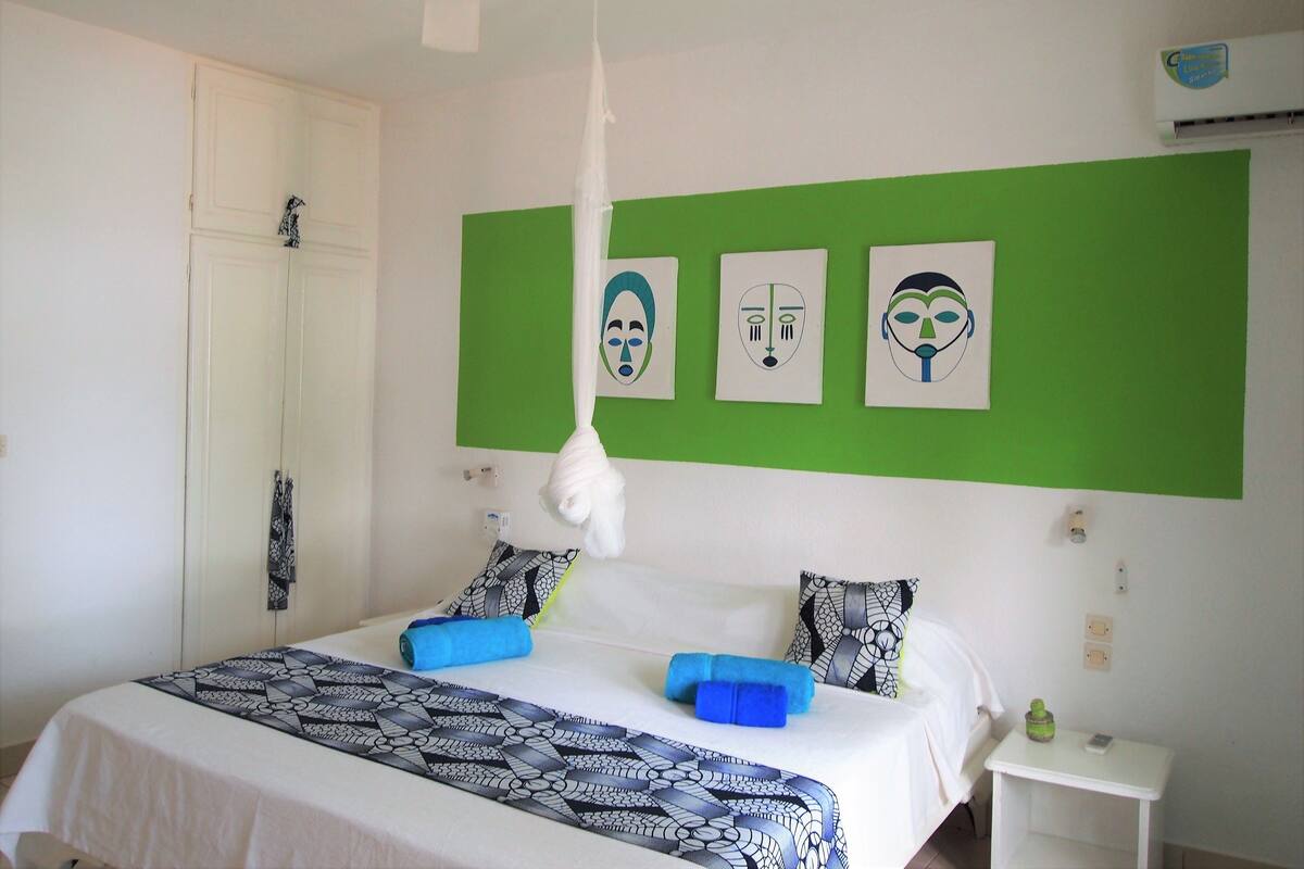 Une chambre à coucher comprenant un lit, des oreillers, une table de chevet et un mur orné de trois œuvres d’art encadrées.