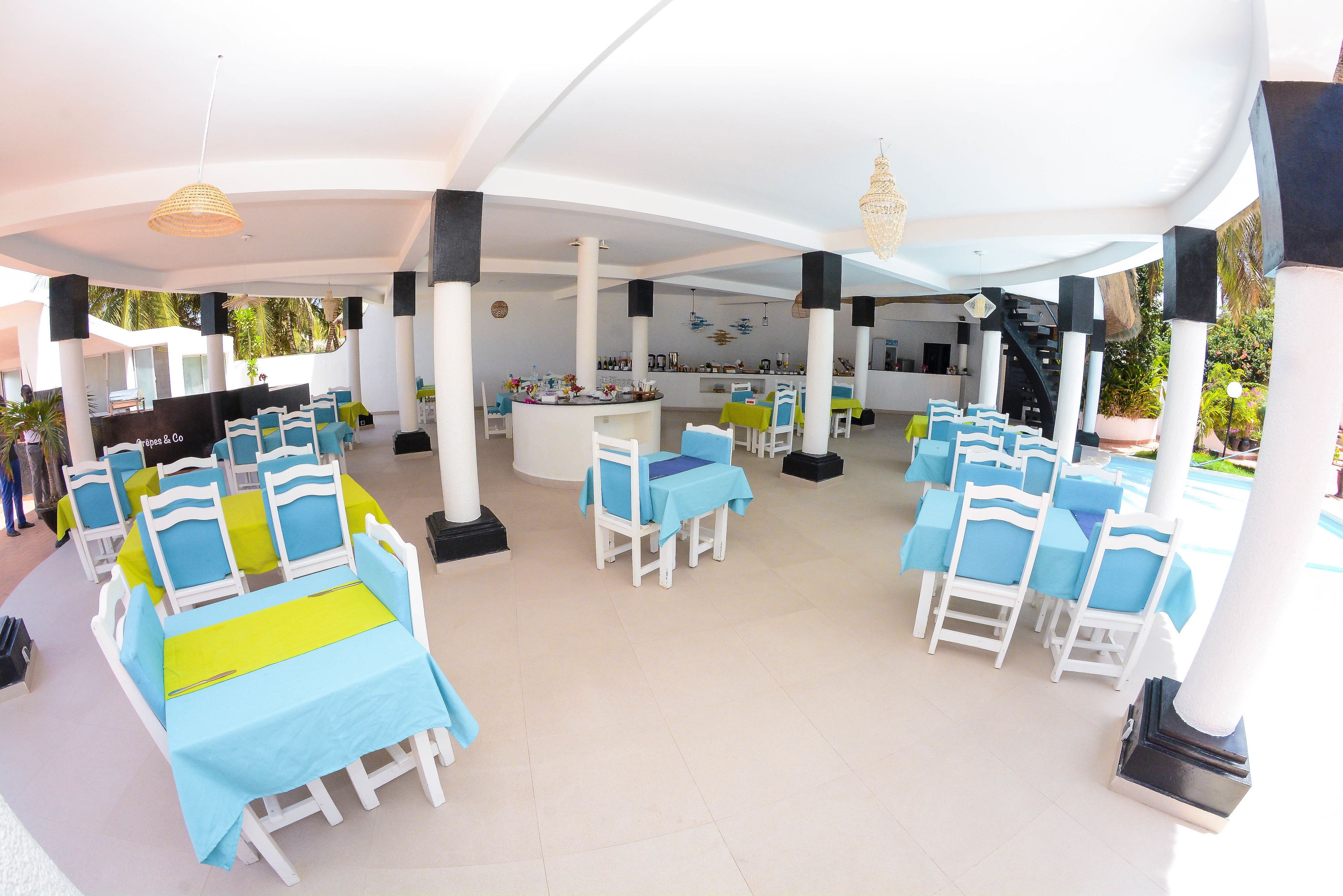 A covered outdoor dining area with white tables and blue chairs, a bar area, and a staircase leading to an upper level.