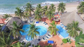 Un resort con varias piscinas, palmeras y acceso a la playa.