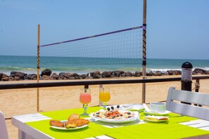 Una mesa con alimentos y bebidas para el desayuno, frente a la playa y con vistas al océano.