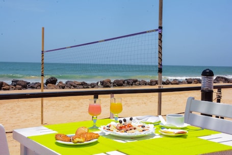 A table with breakfast items and drinks on a beach overlooking the ocean.