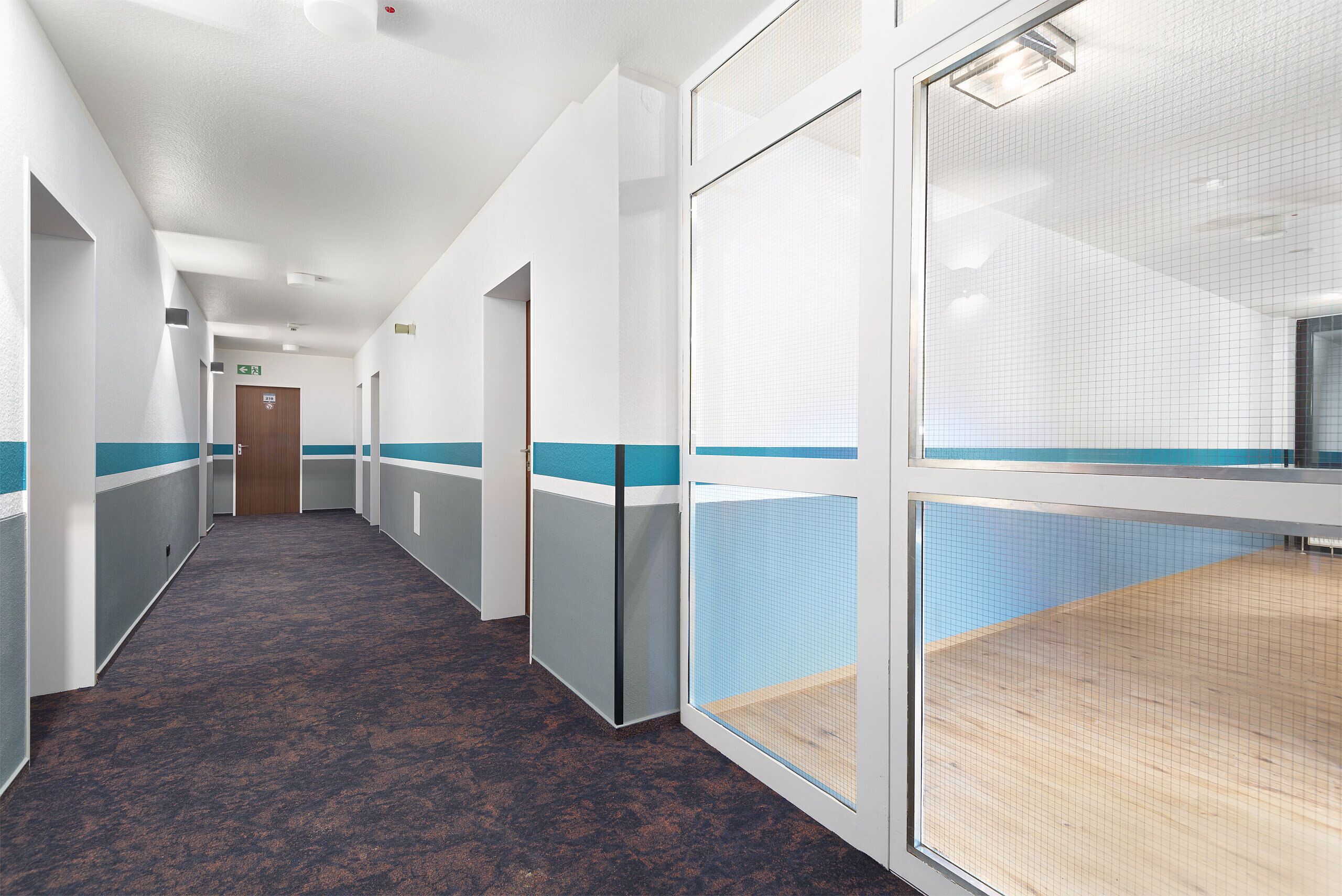 A hallway with a carpeted floor, white walls with blue trim, and a wooden door at the end.