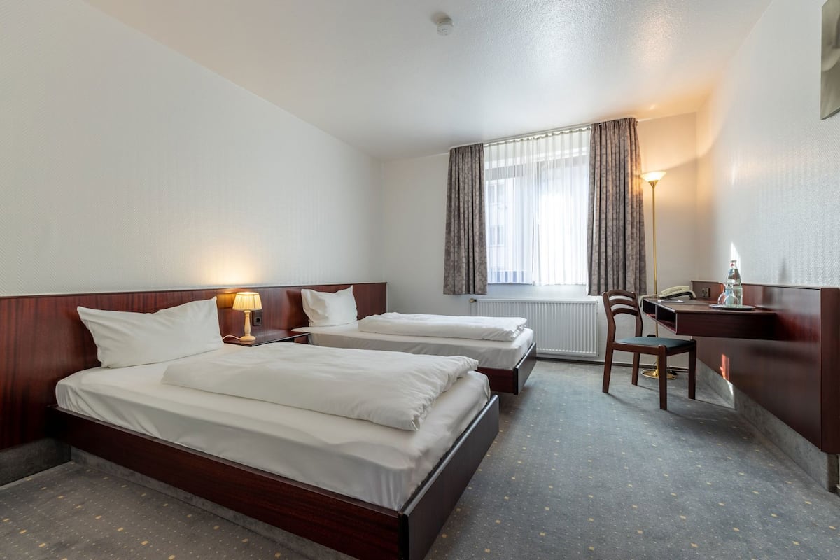 Een hotelkamer met twee bedden, een bureau, een stoel, een lamp en een raam met gordijnen.