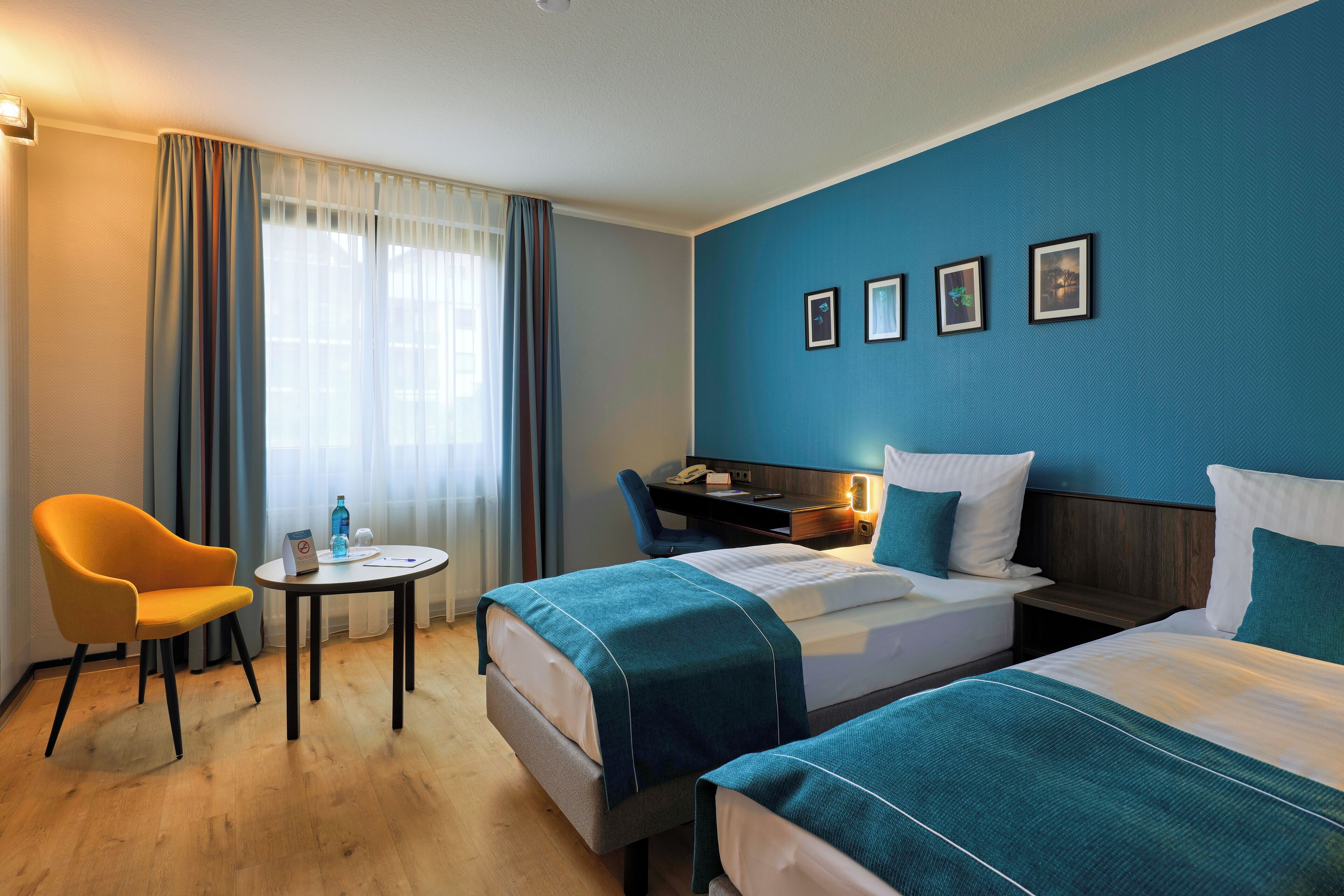 A hotel room with two beds, a desk, a chair, and a small table.