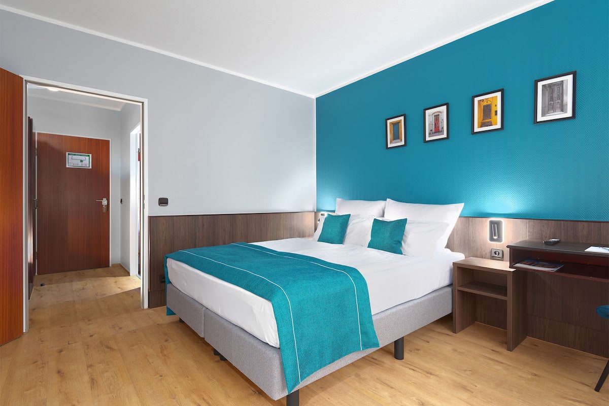 Een hotelkamer met een bed, een nachtkastje, een bureau en een muur met ingekaderde foto's.