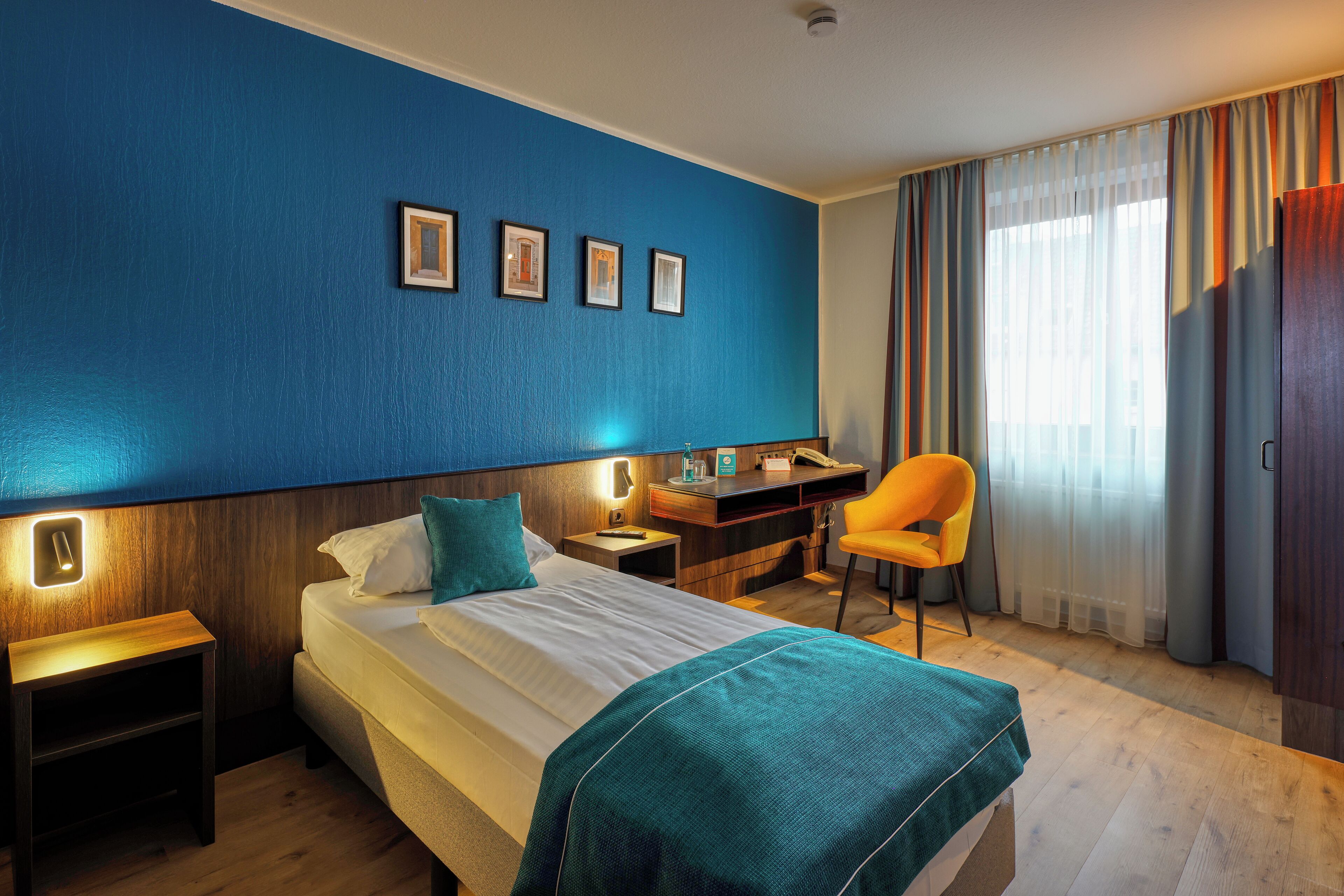 Una habitación de hotel con cama, escritorio, silla y ventana con cortinas.