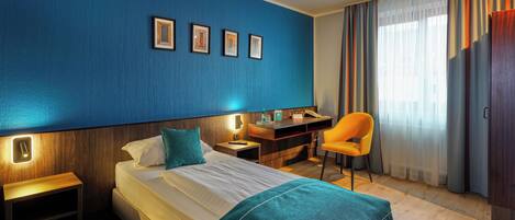 Una habitación de hotel con cama, escritorio, silla y ventana con cortinas.