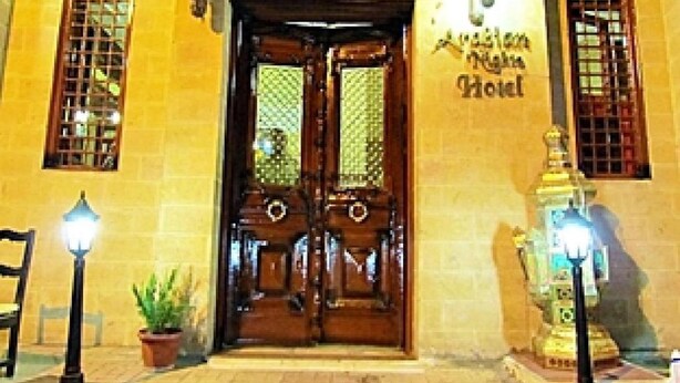 A hotel entrance with a wooden double door, two windows with decorative grills, and a sign above the door. - Arabian Nights Hotel (Cairo)