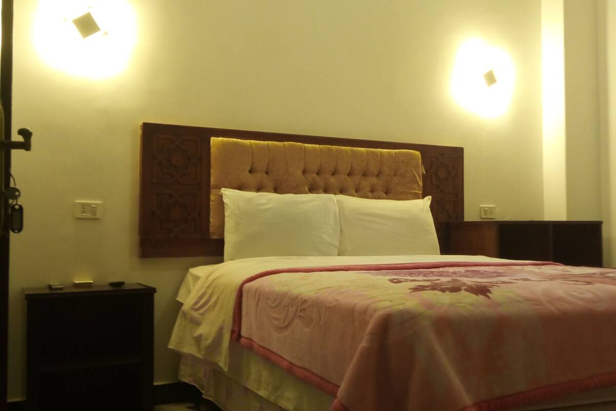 A bedroom with a tufted headboard, two bedside tables, a bed with a floral bedspread, and wall-mounted lights.