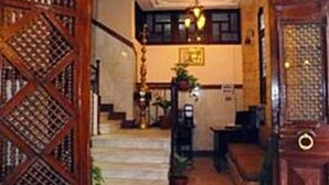 A grand staircase leading to a landing with a chandelier, wooden paneling, and a reception area with a desk and plants. - Arabian Nights Hotel (Cairo)