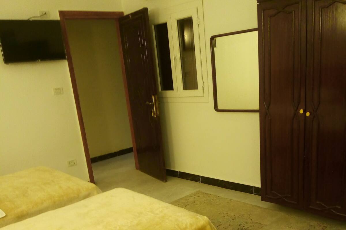 A hotel room with two beds, a wardrobe, a television, and a door leading to another room.