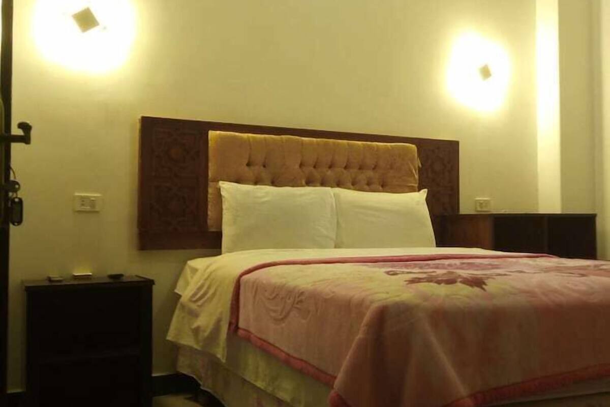 A neatly made bed with a headboard, a bedside table, and two wall-mounted lights.
