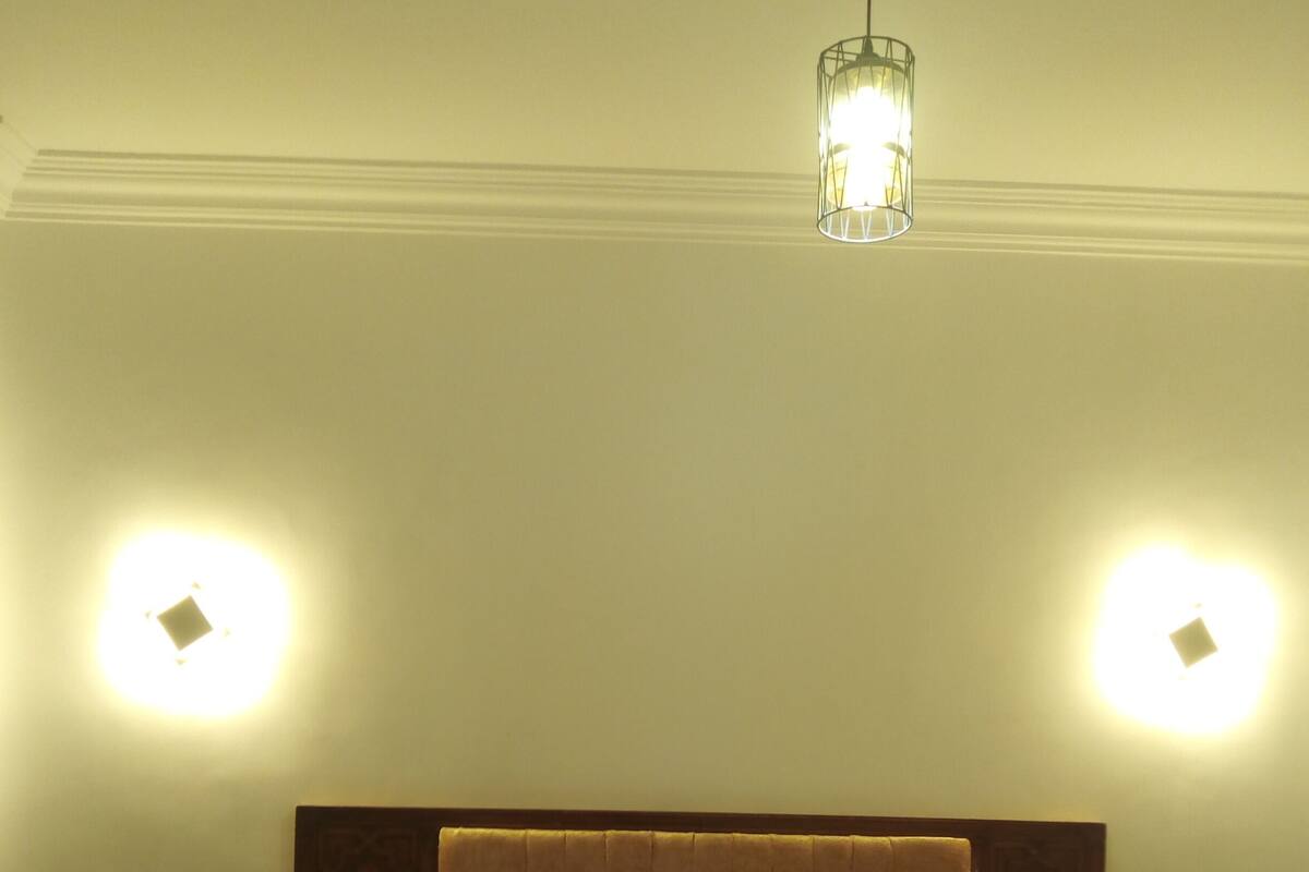 A hotel room with a tufted headboard, two bedside tables, a bed with a floral bedspread, and two wall-mounted lights.