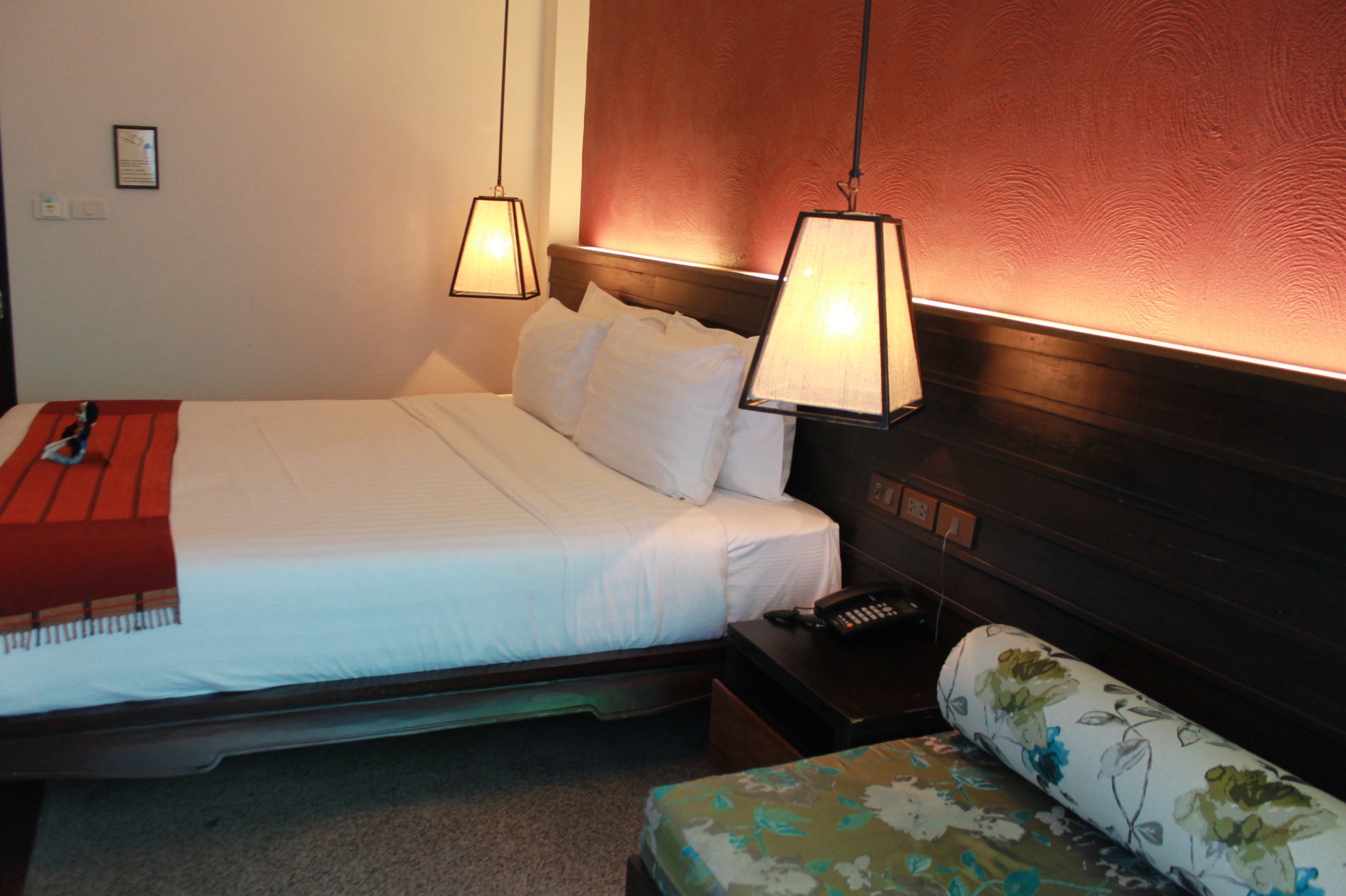 Una habitación de hotel con cama, lámparas de noche, teléfono y una silla estampada con motivos florales.