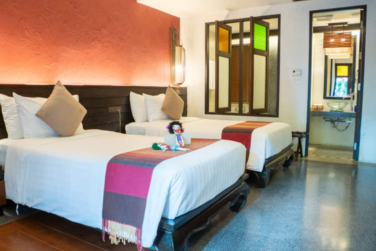 Habitación de hotel con dos camas, cabecero de madera, un espejo y un baño visible a través de una puerta abierta.