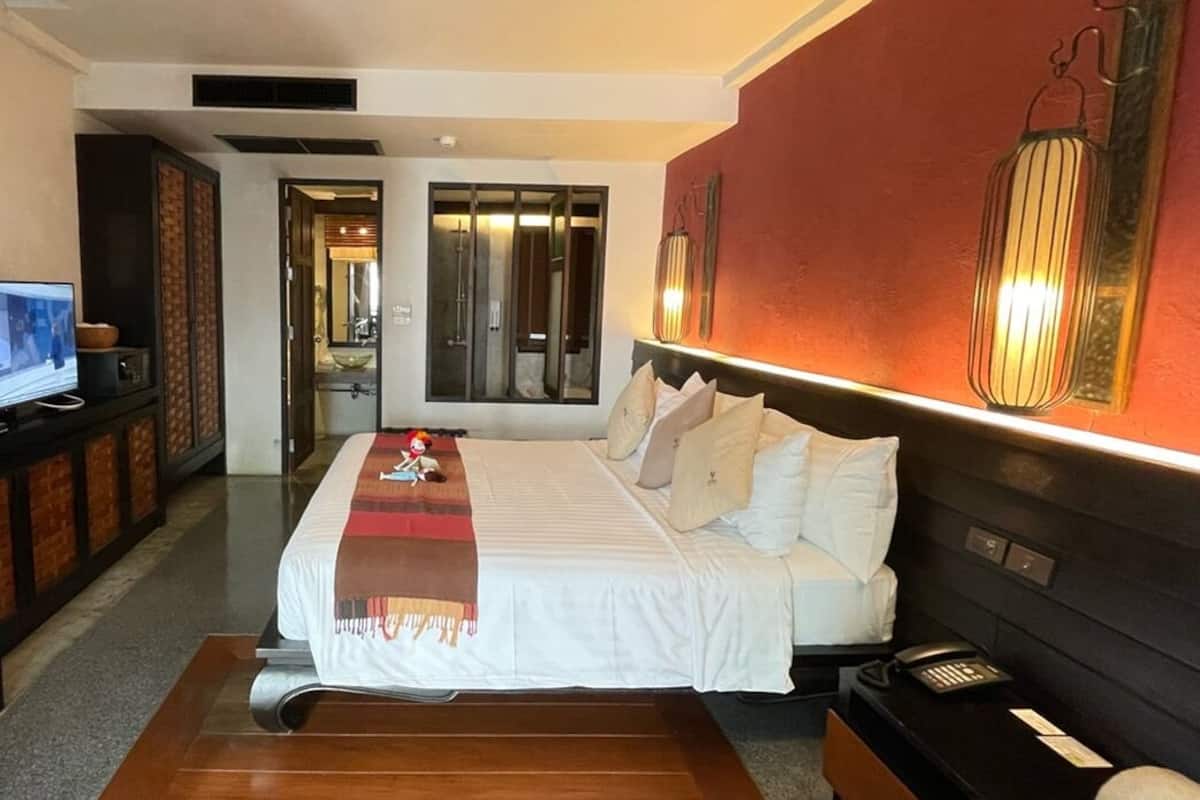 Habitación de hotel con una cama grande, un escritorio con computadora, un televisor y un baño visible a través de una puerta abierta.