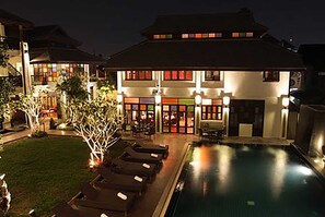 A hotel with a swimming pool, lounge chairs, and a well-lit exterior.
