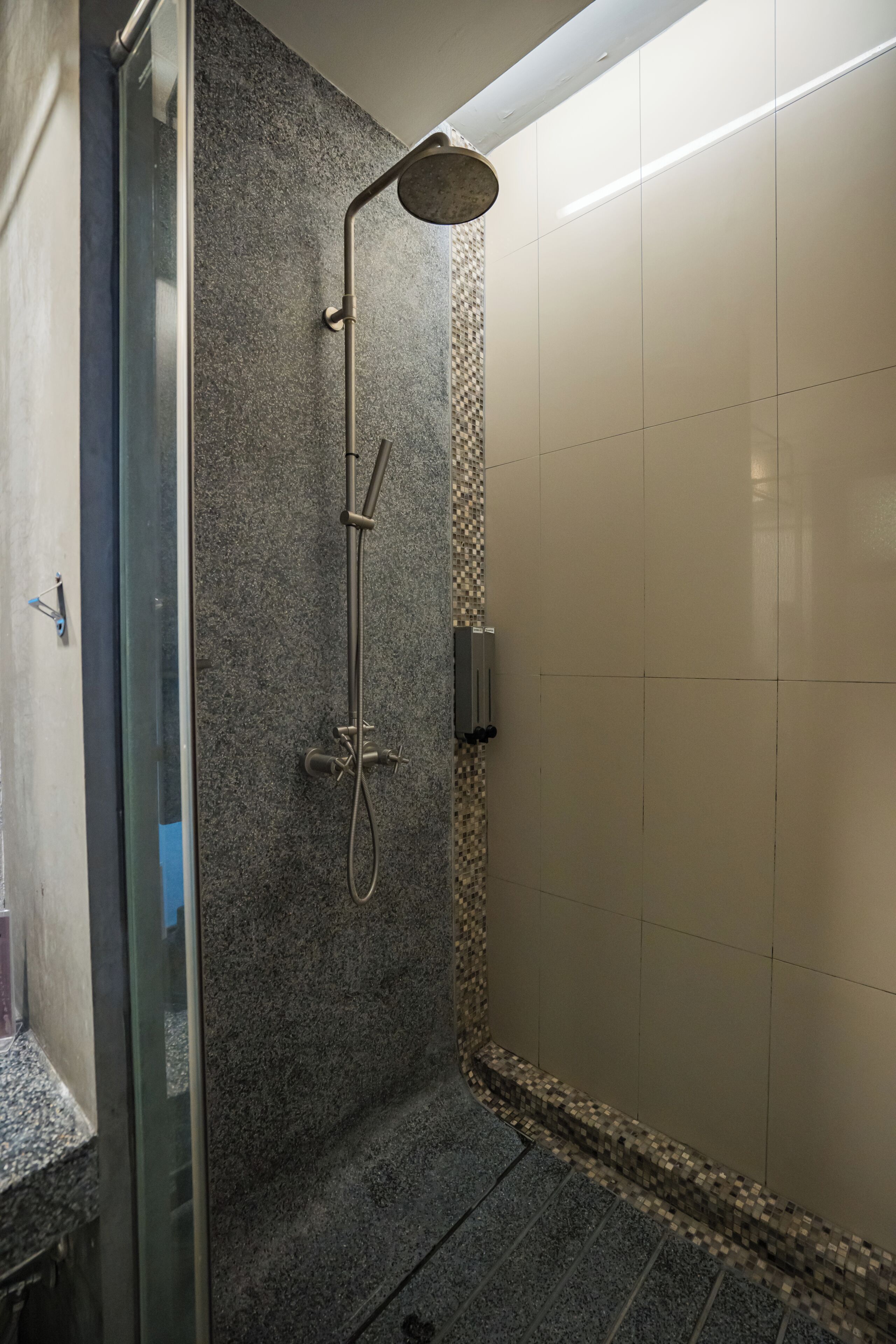 A shower with a handheld showerhead, a wall-mounted control panel, and a tiled floor.
